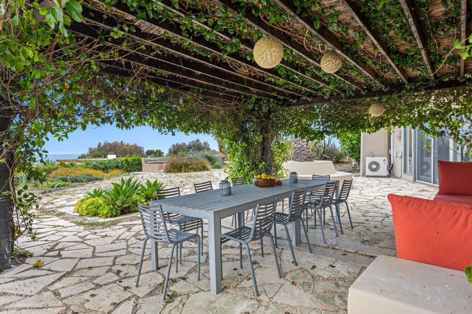 Vine-covered pergola over a stone patio with a dining table