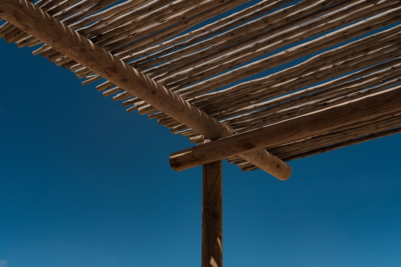Timber pergola slats seen from below against a deep blue sky